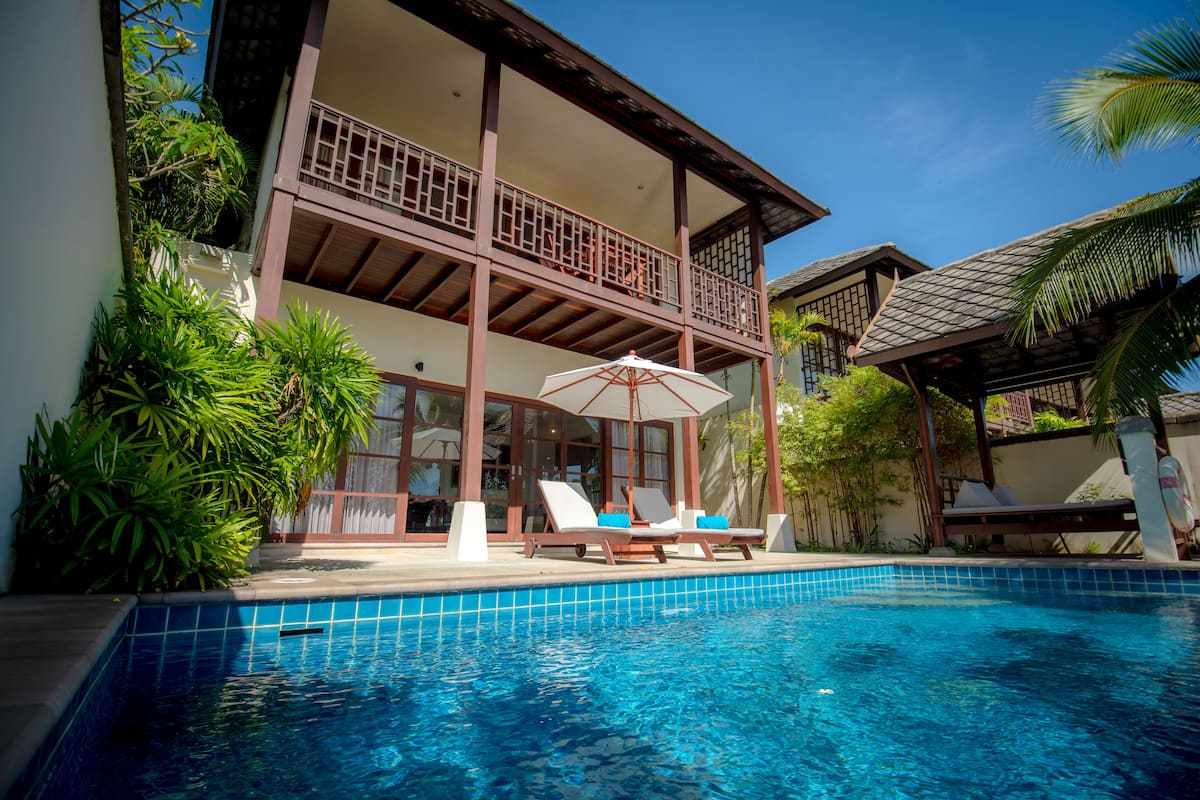 A two-story building with a swimming pool, lounge chairs, and umbrellas.
