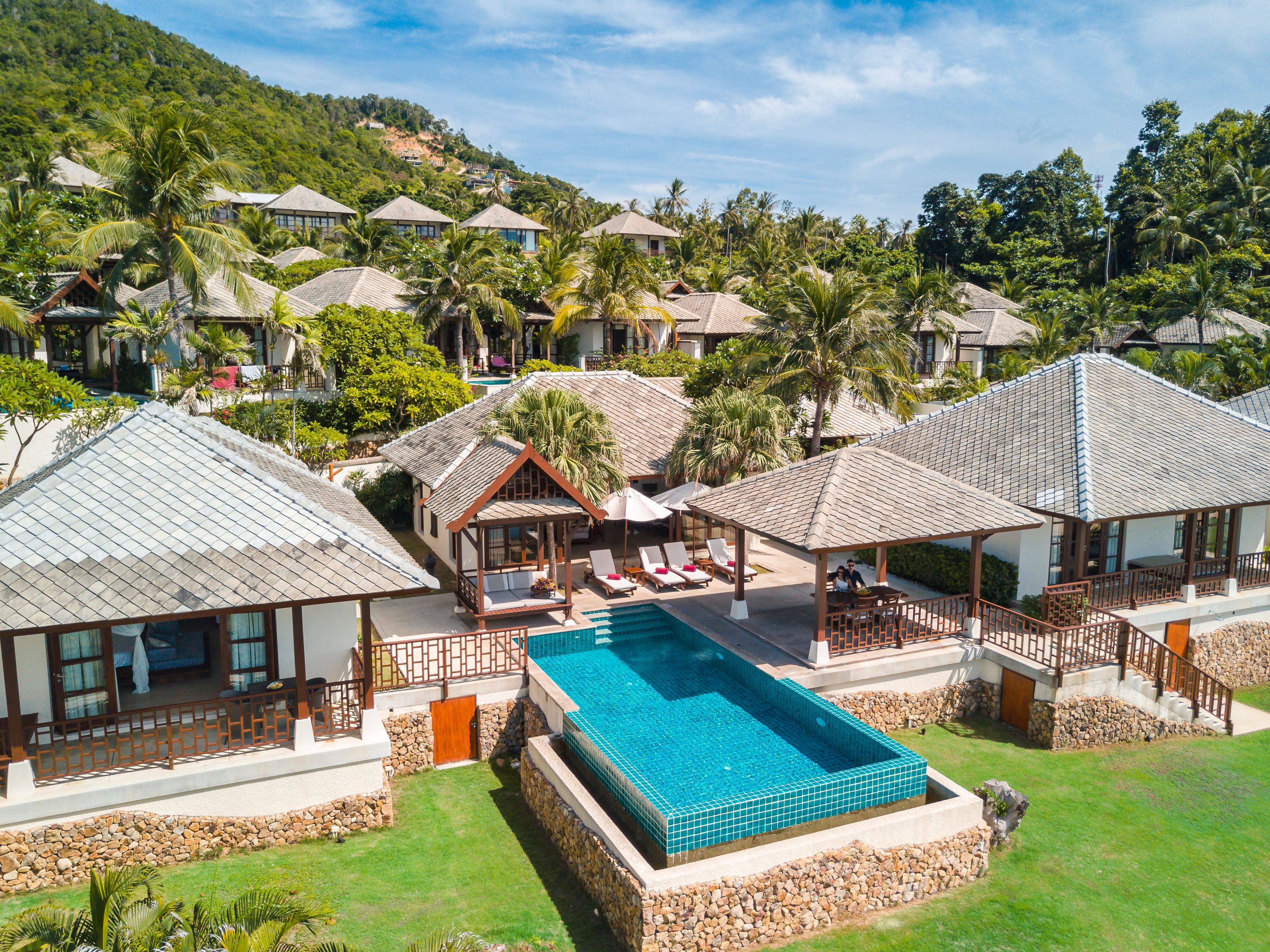 Un complexe hôtelier comprenant plusieurs bâtiments de style bungalow, une piscine centrale et une végétation luxuriante qui entoure l’ensemble du site.