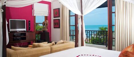A hotel room with a bed, a TV, a sofa, and a balcony with a view of the sea.
