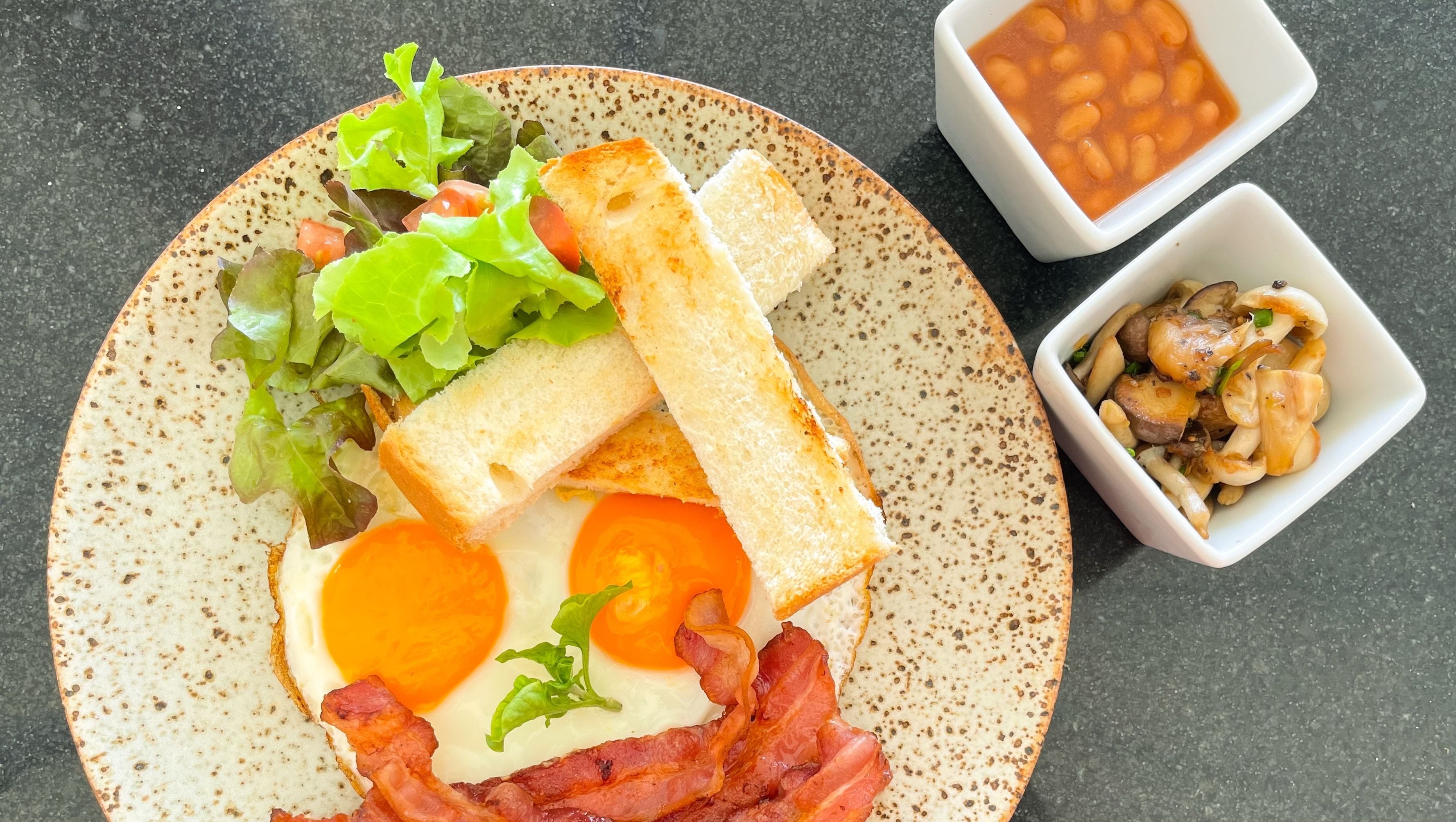 Un plato de desayuno con tostadas, huevos, tocino y ensalada, acompañado de tazones de frijoles y champiñones.
