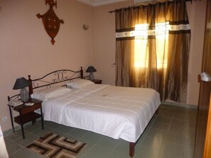 A bedroom with a bed, two bedside tables, a lamp, a wall clock, and a patterned rug.