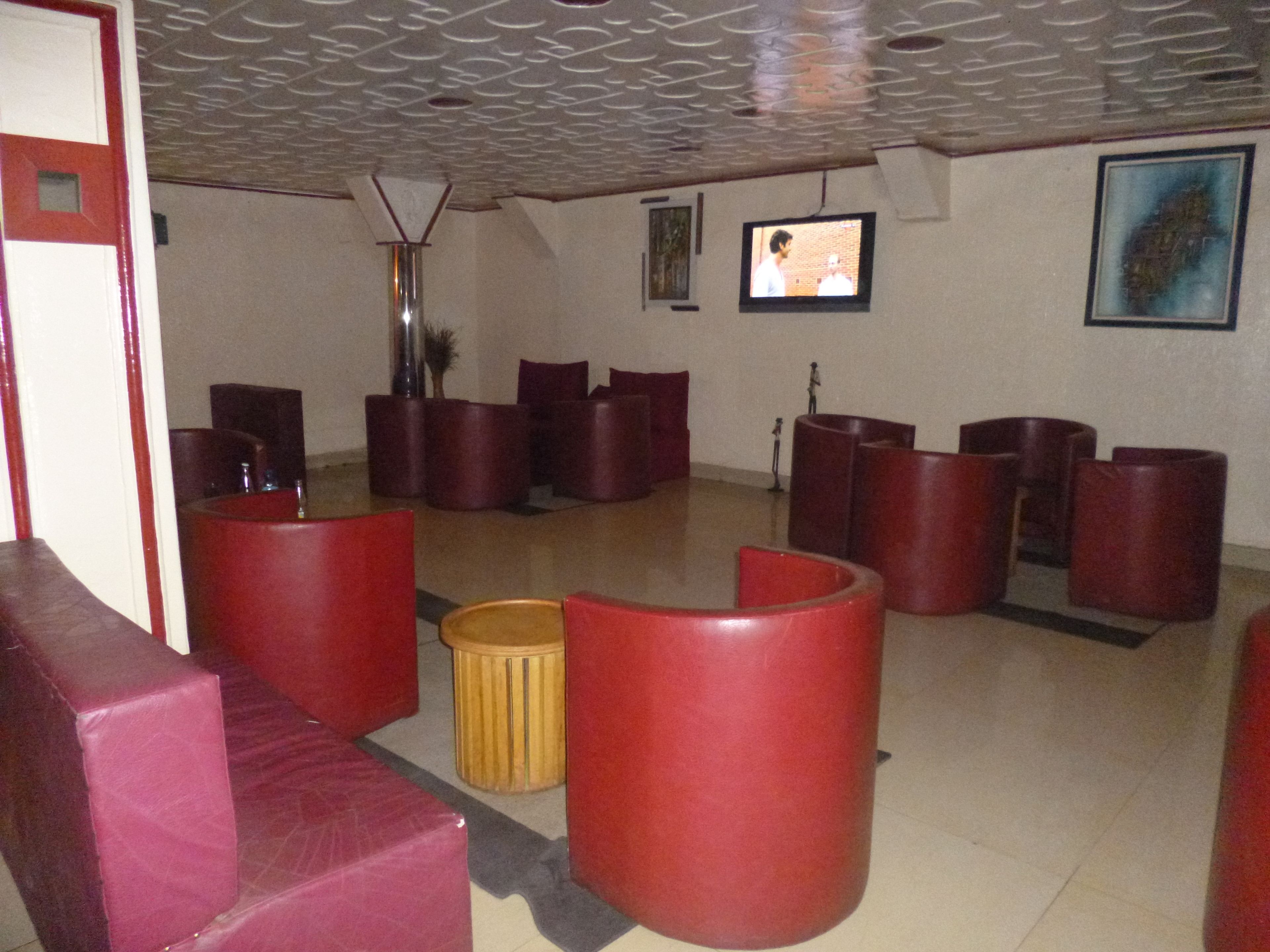 A lobby with red cushioned seating, a small trash bin, a television on the wall, and a framed picture.