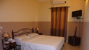 Hotellihuone, jossa on sänky, kaksi yöpöytää valaisimineen, taulutelevisio ja pieni kaiutin.