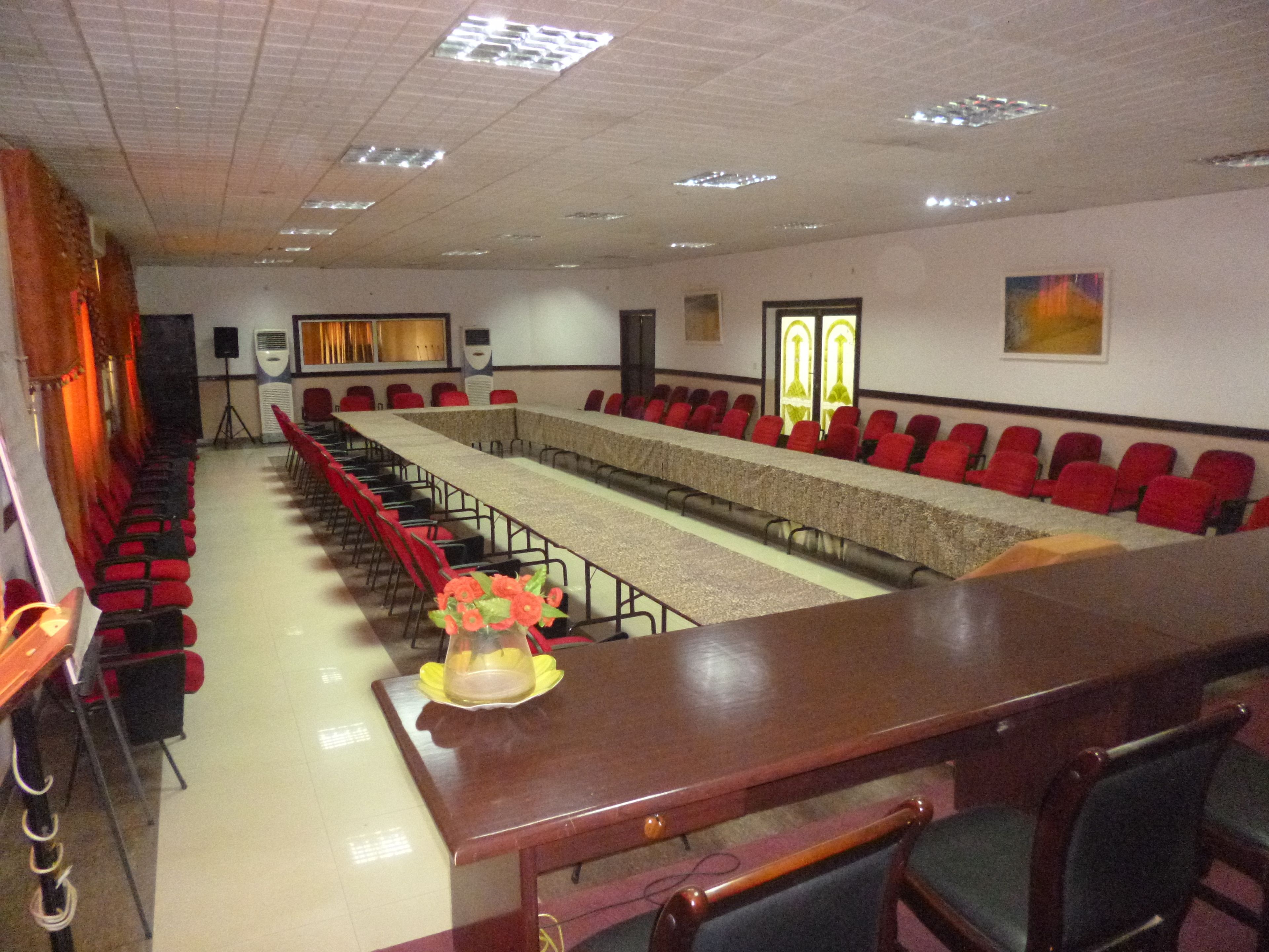A conference room with a long table, rows of red chairs, and a stage area.