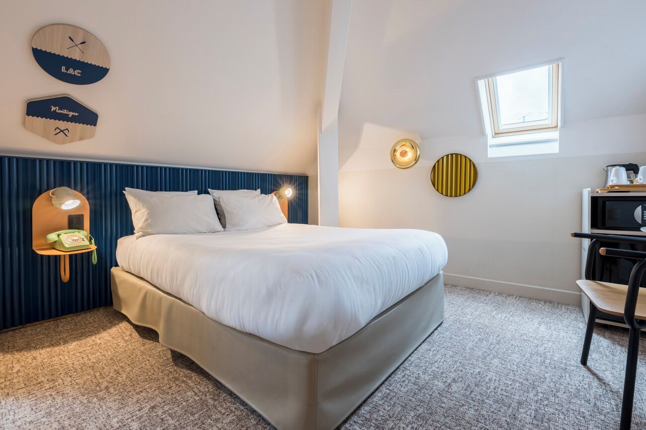 Une chambre d’hôtel équipée d’un lit, d’un bureau, d’une chaise, d’une fenêtre et d’horloges fixées au mur.