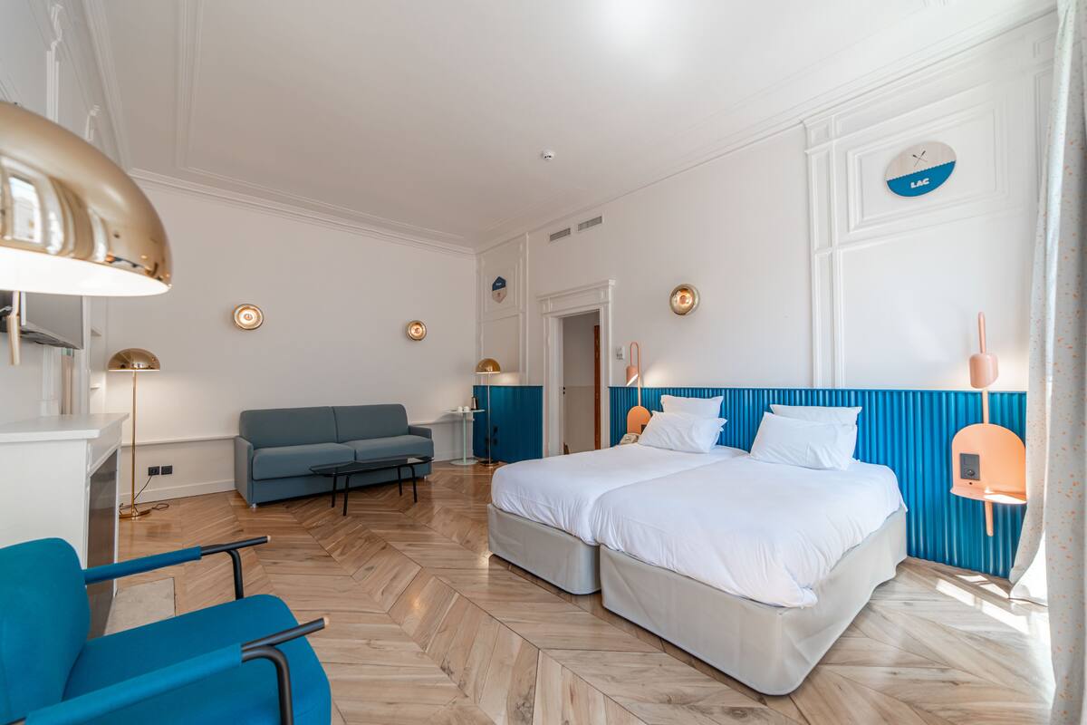 Une chambre moderne avec un grand lit, un mur d’accent bleu et un parquet en bois disposé en chevrons.