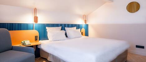 Una habitación de hotel moderna con una cama grande, una mesita de noche con teléfono y una pared azul decorativa.