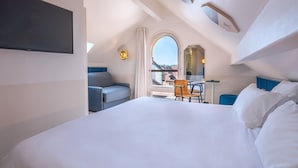 A modern hotel room with a large bed, a desk, and a chair. There is a TV mounted on the wall and a window with a view of the city. - Hôtel du Palais de l'Isle (Annecy)