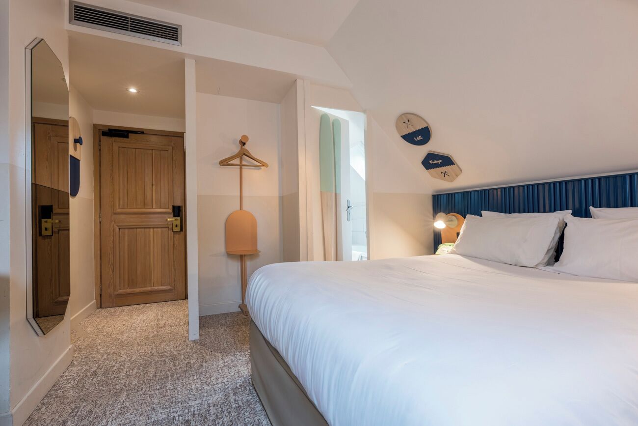 A bedroom with a bed, a wooden door, a hanging light, and a wall clock.