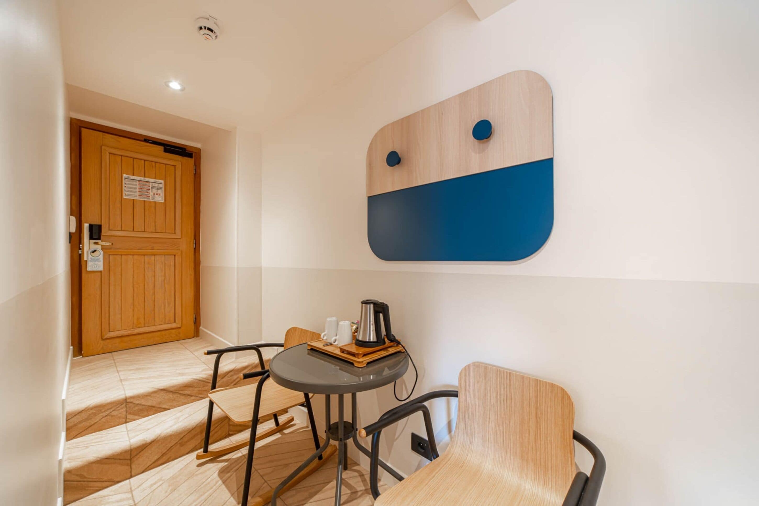 Una habitación de hotel con una puerta de madera, una mesita con una cafetera y una silla.