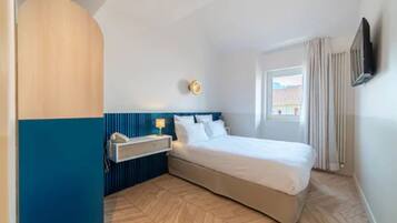 Moderni hotellihuone, jossa on suuri sänky, yöpöytä lampun kanssa, seinälle asennettu televisio ja ikkuna, jossa on verhot.