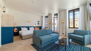 A modern hotel room with a bed, two sofas, a coffee table, and a view of the city through large windows. - Hôtel du Palais de l'Isle (Annecy)
