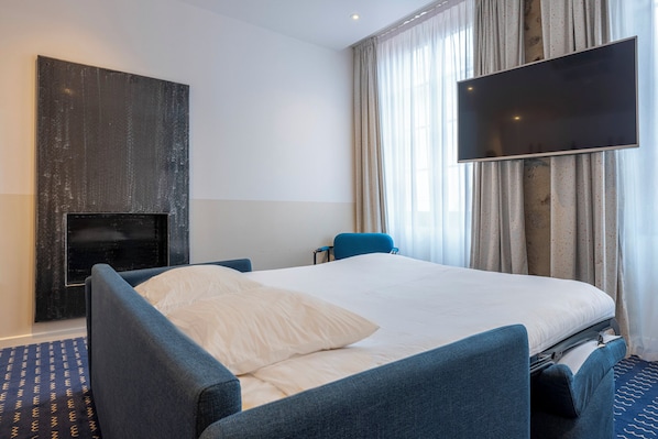 A hotel room with a bed, a chair, a flat-screen TV, and a fireplace.