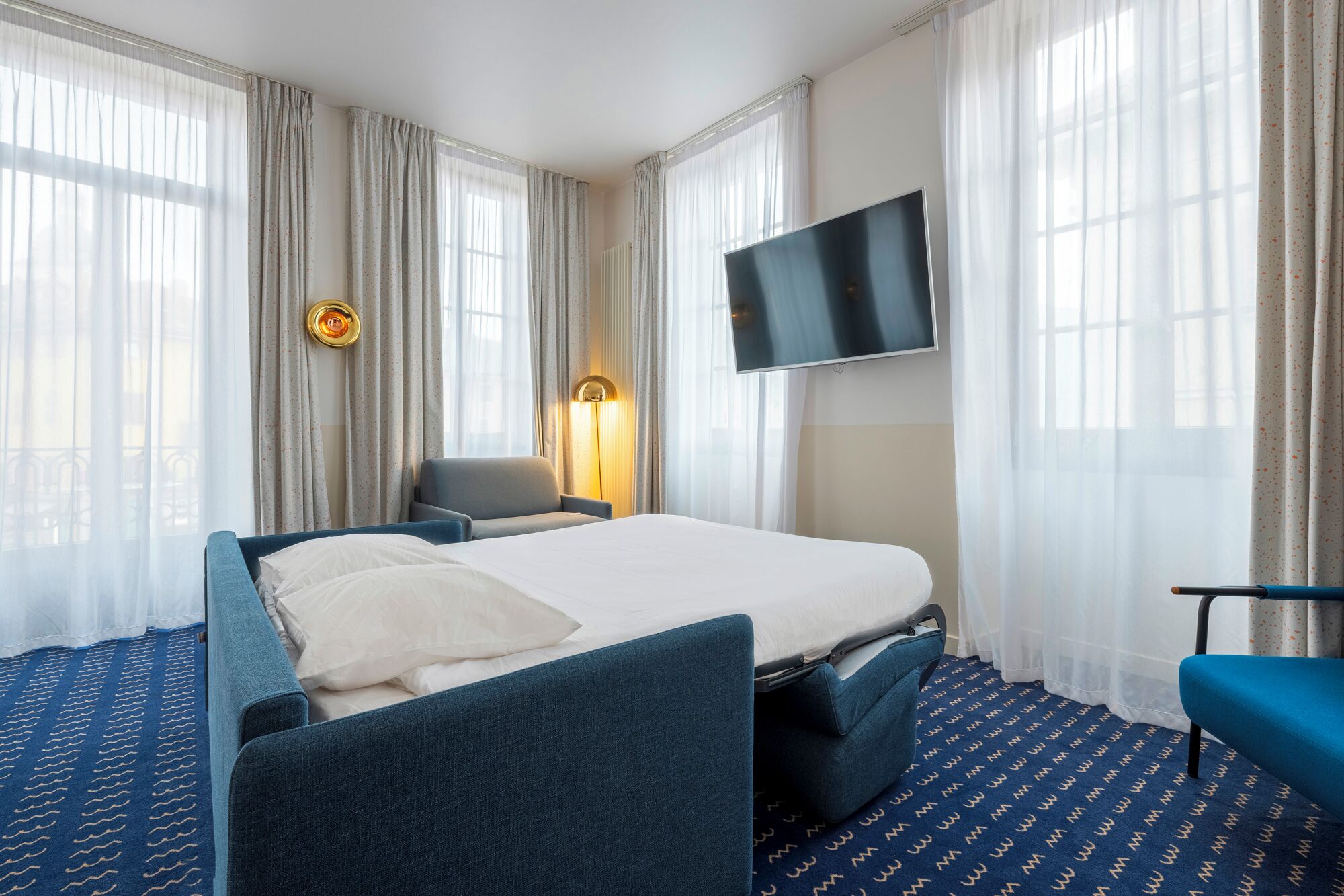 Una habitación de hotel con cama, una silla, televisor y lámpara.