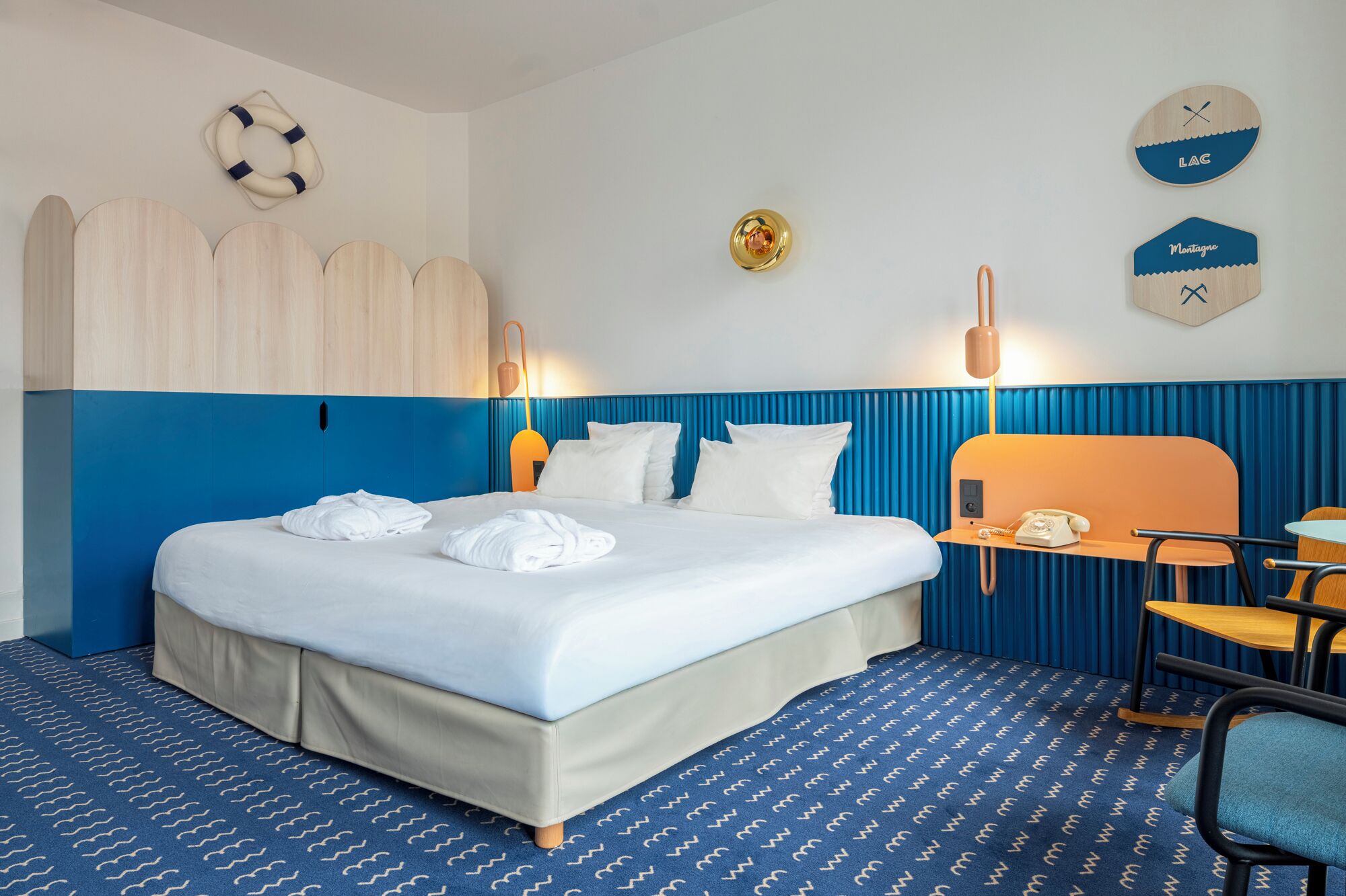 Une chambre d’hôtel avec un lit, un bureau, une chaise, une lampe et une horloge murale.