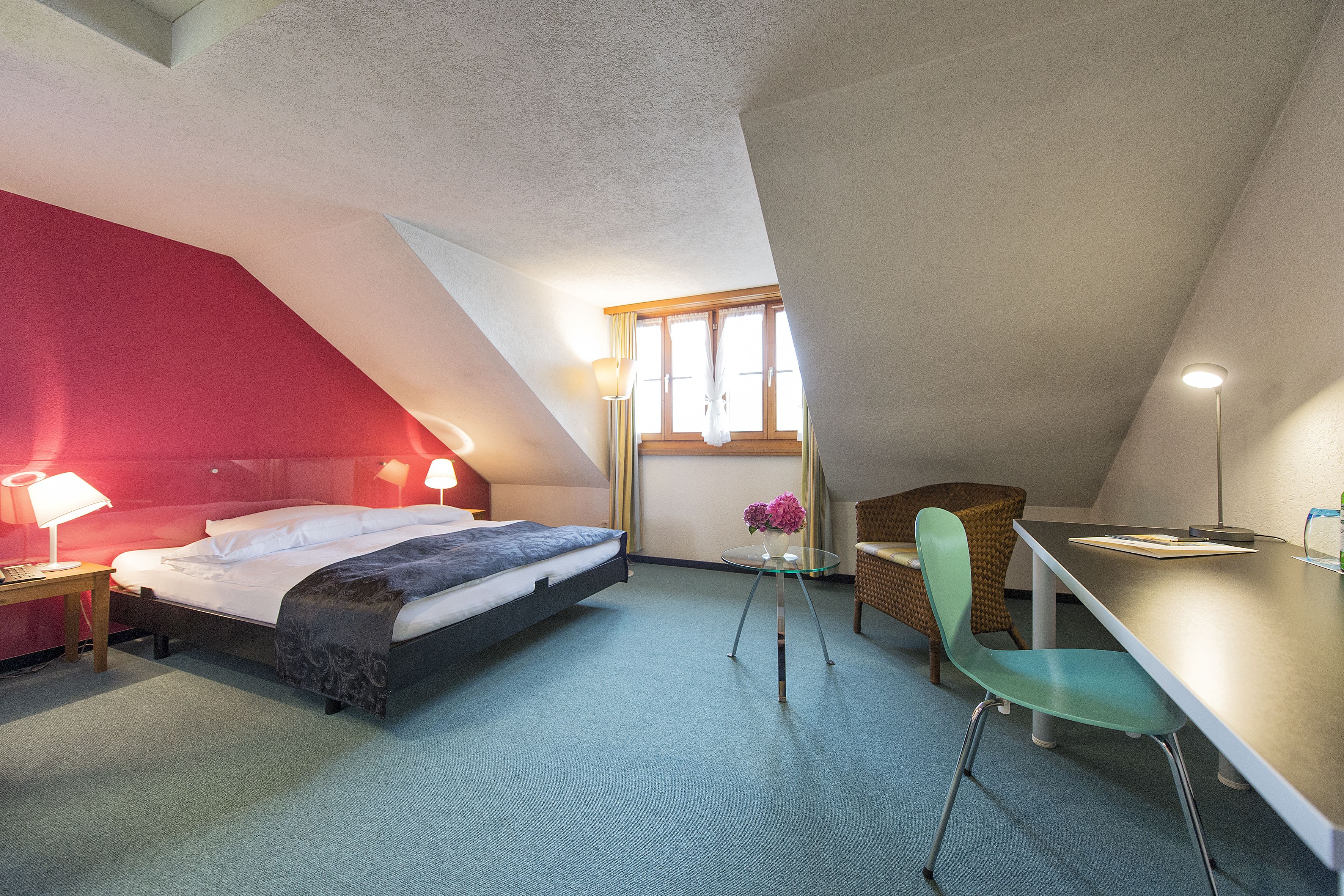 Une chambre à coucher comprenant un lit, une table de chevet, une lampe, une chaise et une petite table sur laquelle est posé un vase.