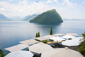 A lakeside view with umbrellas and outdoor seating. - See- und Seminarhotel FloraAlpina (Vitznau)
