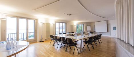 A spacious conference room with a long table, black chairs, and large windows.