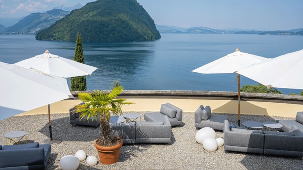 A terrace with outdoor seating, a potted plant, and a view of a lake and a mountain. - See- und Seminarhotel FloraAlpina (Vitznau)