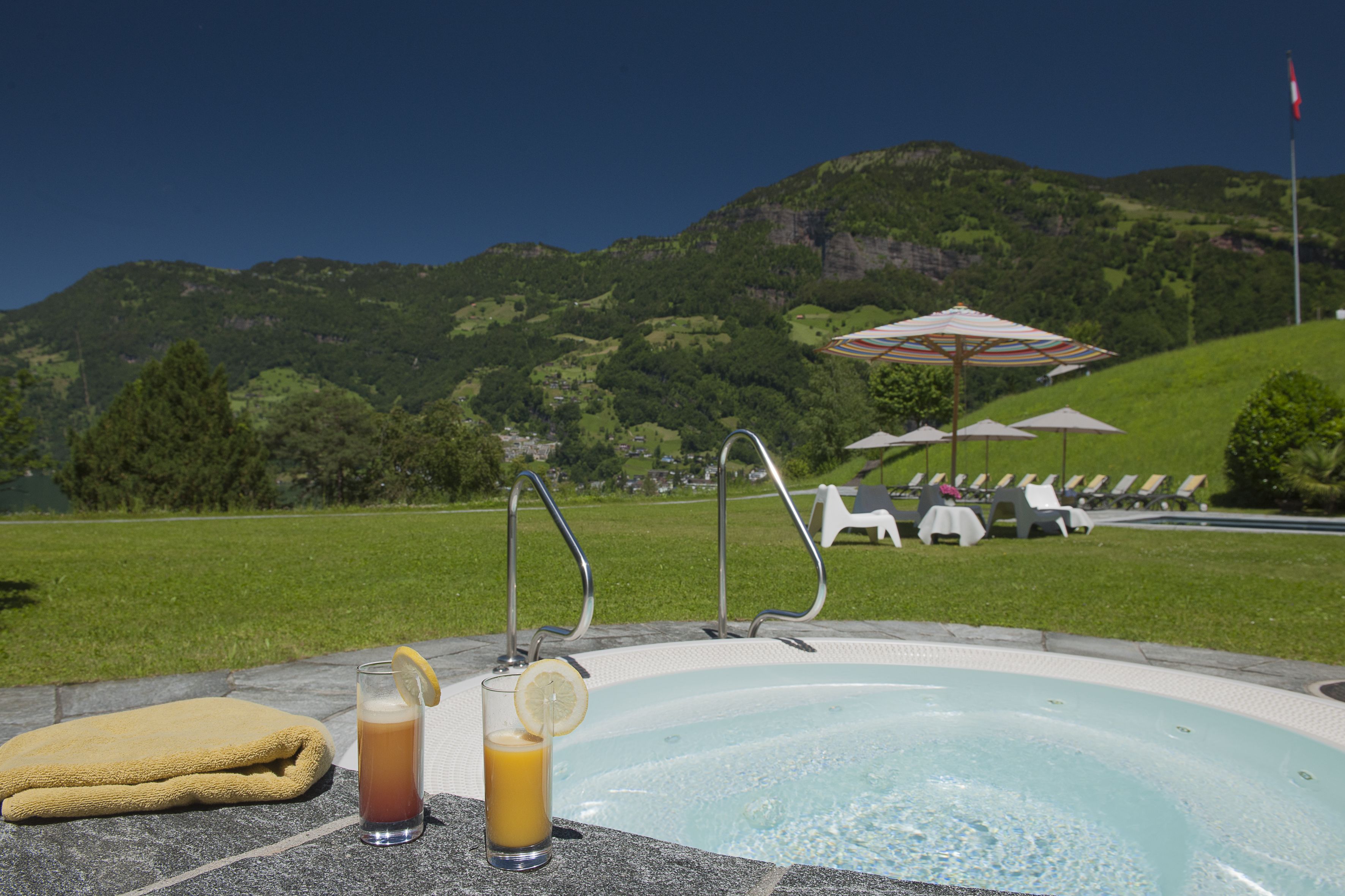 Zona de piscina con una limonada, una toalla y sillones de playa con sombrillas.