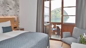 A hotel room with a bed, a sofa, a balcony with a table and chairs, and a view of a lake and mountains. - See- und Seminarhotel FloraAlpina (Vitznau)