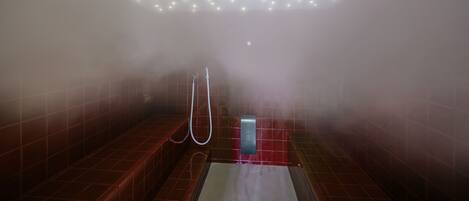 A steam room with tiled walls, a bench, and a showerhead.