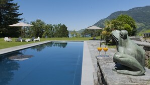 A swimming pool with lounge chairs and a stone frog statue. - See- und Seminarhotel FloraAlpina (Vitznau)