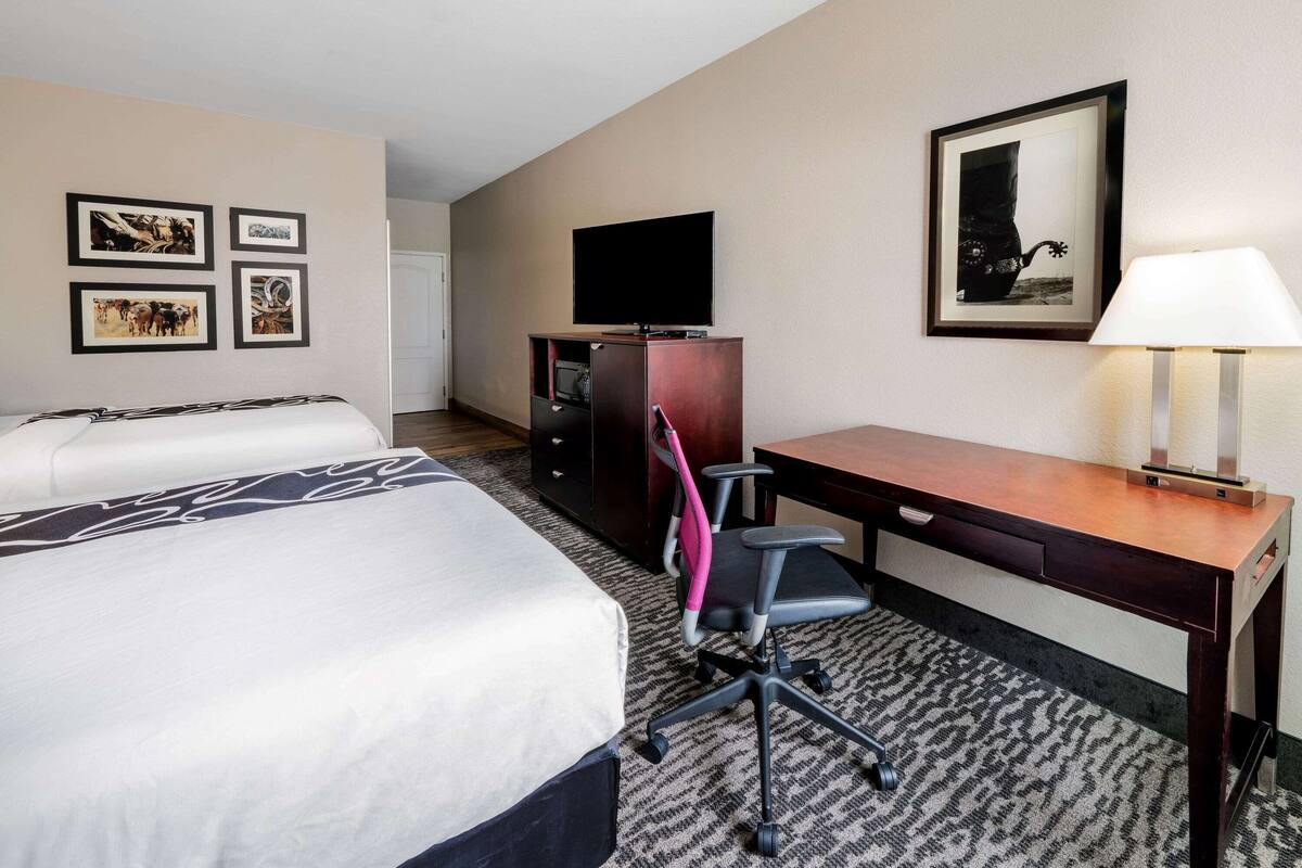 Ein Hotelzimmer mit einem großen Bett, einem Schreibtisch, einem Sessel, einem Fernseher und gerahmten Bildern an der Wand.
