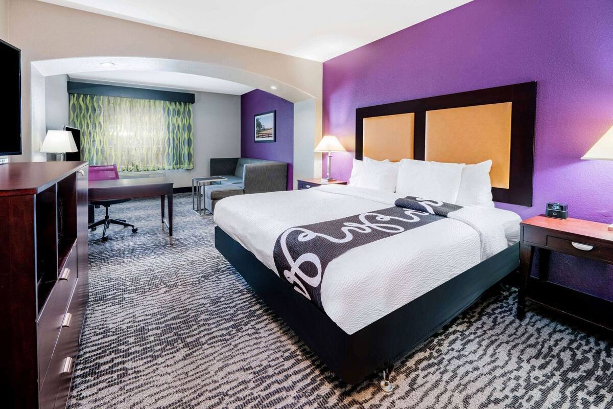 Ein Hotelzimmer mit einem großen Bett, einem Schreibtisch, einem Sessel und einem Fernseher.