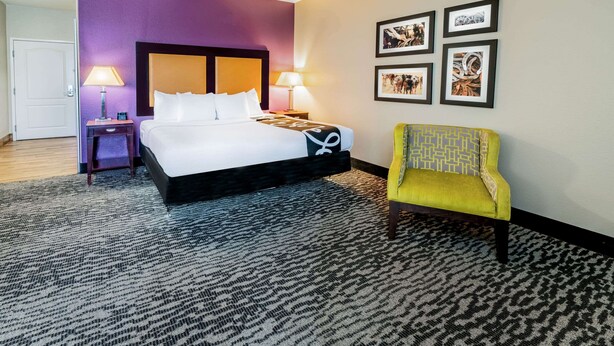 A hotel room with a bed, a nightstand, a chair, and framed pictures on the wall. - La Quinta Inn & Suites by Wyndham DFW Airport West - Bedford (Bedford)