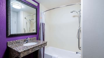 A bathroom with a granite sink, a white bathtub, and a shower with a curved glass door.