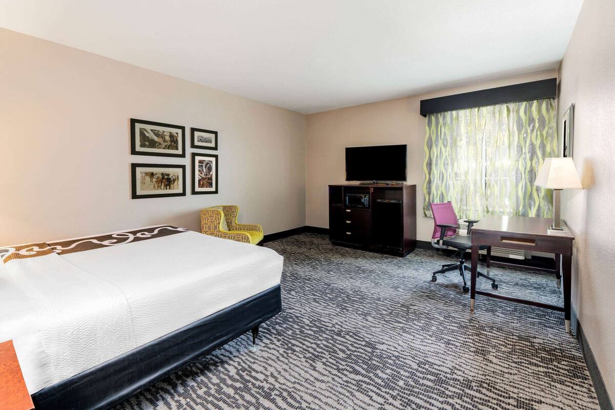 Ein Hotelzimmer mit Bett, Schreibtisch, Stuhl, Fernseher und gerahmten Bildern an der Wand.