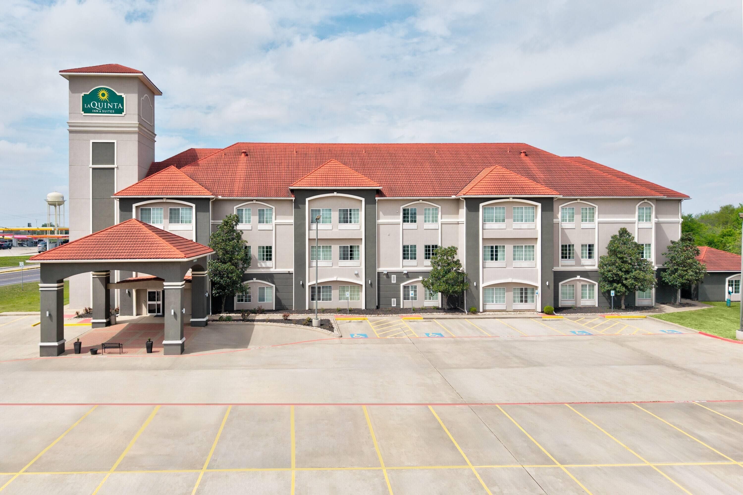A La Quinta Inn & Suites hotel with a central entrance, a parking lot, and a tower.