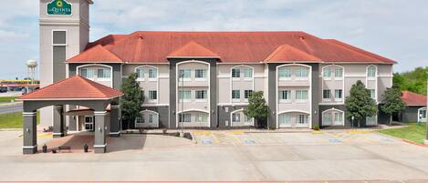 A La Quinta Inn & Suites hotel with a central entrance, a parking lot, and a tower.