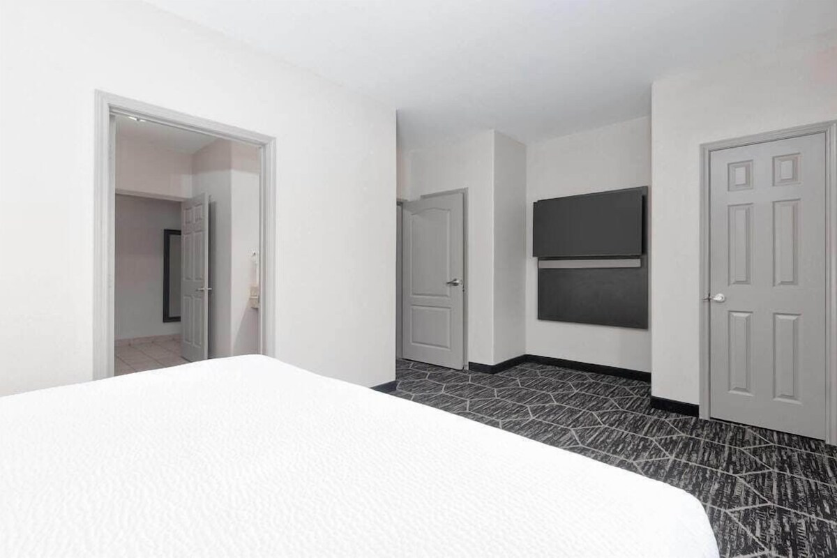 Une chambre d’hôtel avec un lit, une porte, un téléviseur fixé au mur et un sol carrelé.