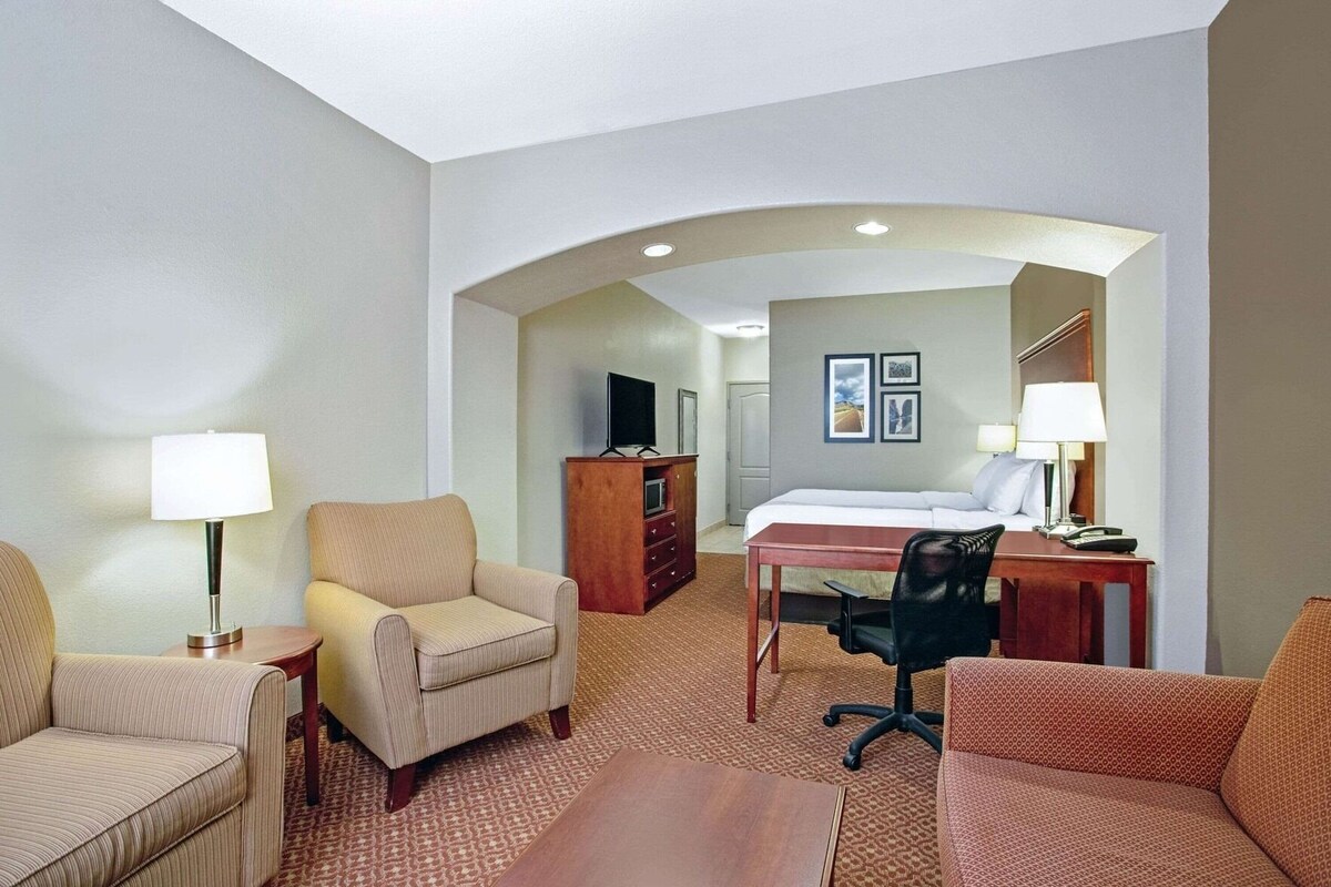 Une chambre d’hôtel comprenant un lit, un bureau, deux fauteuils, un canapé, une télévision et une commode.