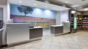 Un área de recepción con dos mostradores, un mural de un árbol y un campo, y un refrigerador con bebidas.