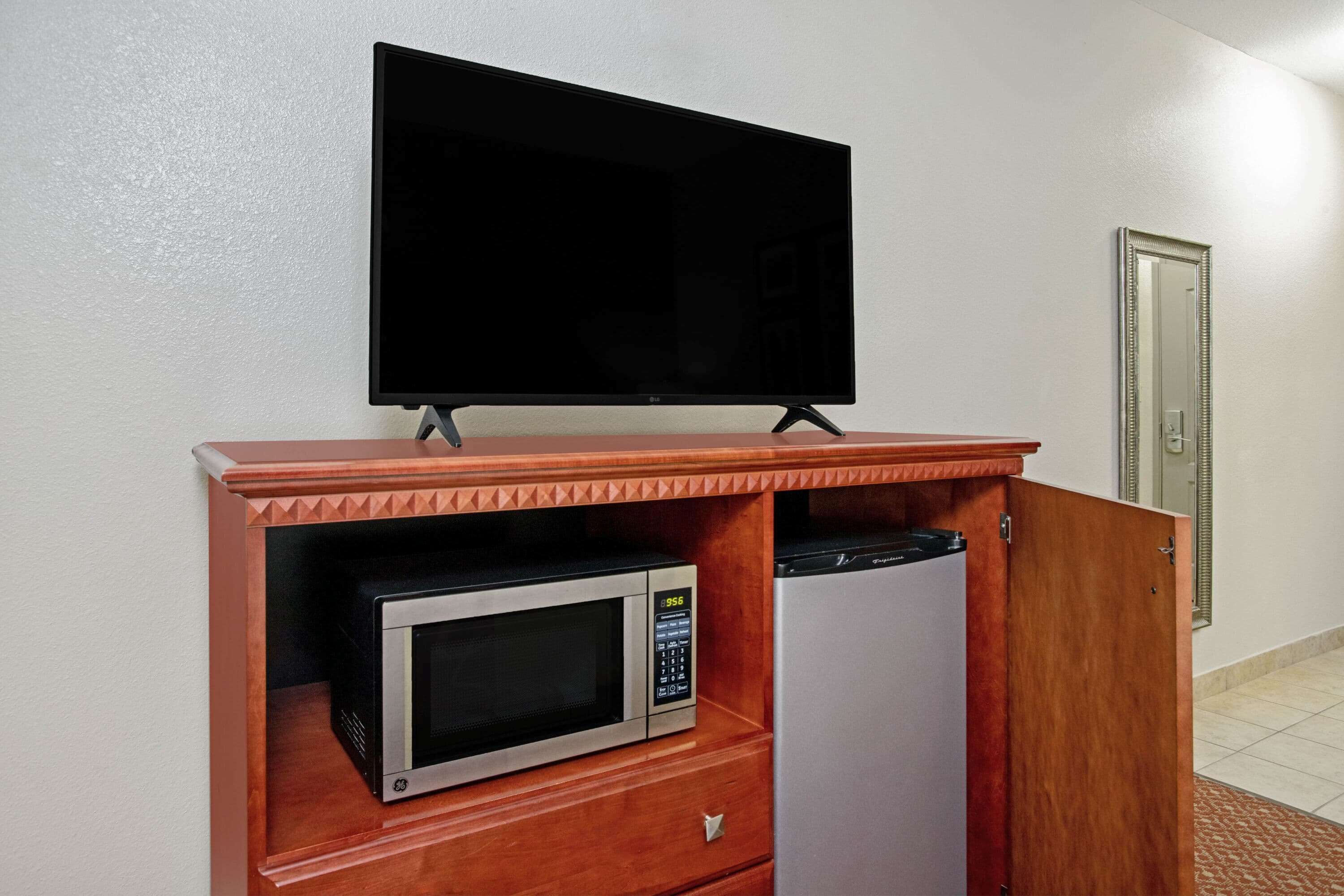 A kitchenette with a microwave, refrigerator, and a flat-screen TV on a wooden cabinet.