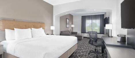 A hotel room with a large bed, a desk, a chair, a television, and a window with curtains.