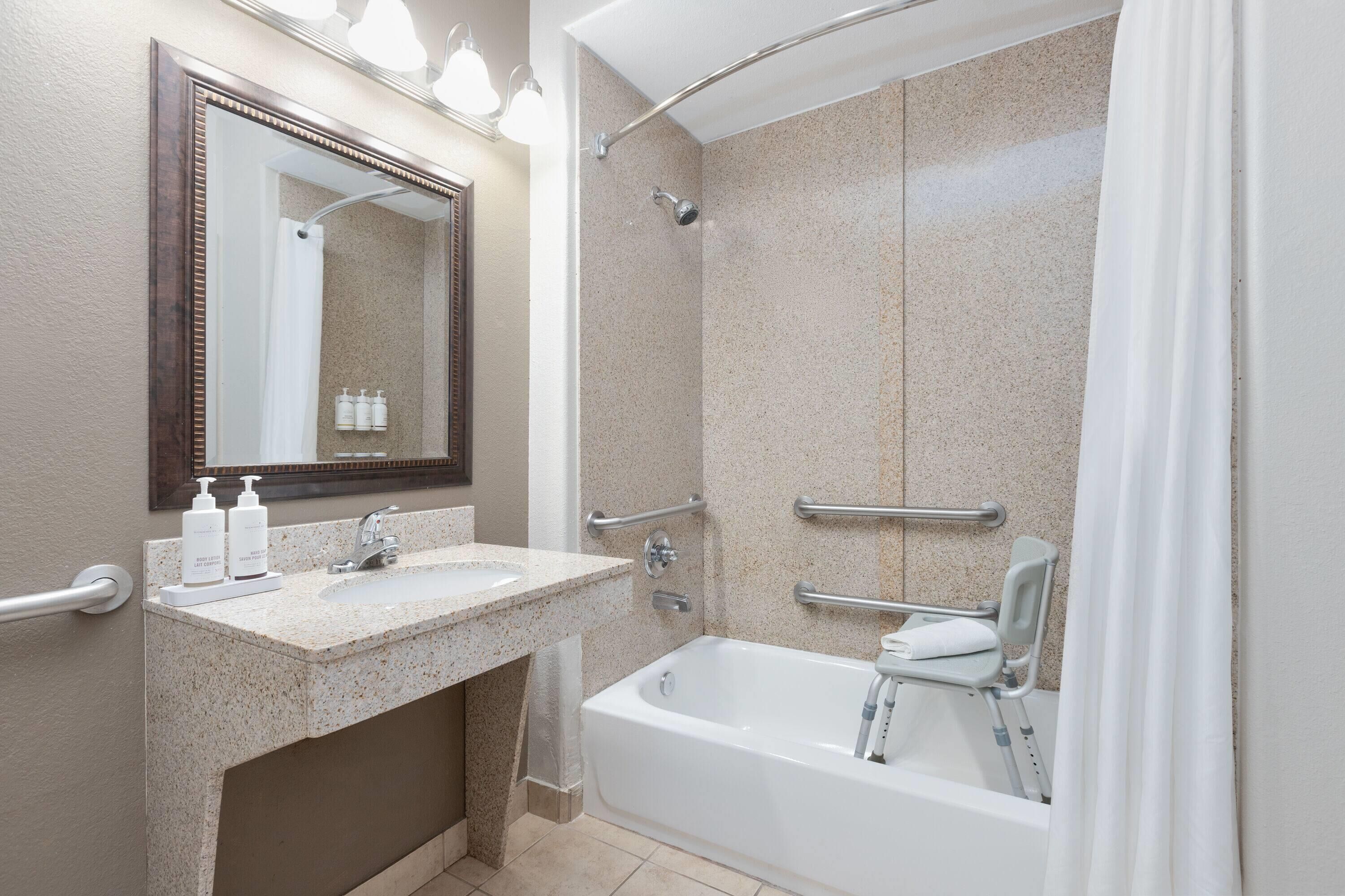 A bathroom with a bathtub, a shower, a sink with hand soap, and a mirror.