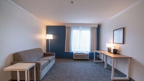 A hotel room with a sofa, a small table, a lamp, and a window with curtains. - Spark by Hilton Brandon (Brandon)
