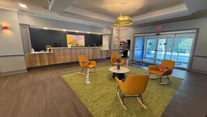 A reception area with a wooden reception desk, yellow chairs, a green rug, and a large window with a view of the outdoors. - Spark by Hilton Brandon (Brandon)