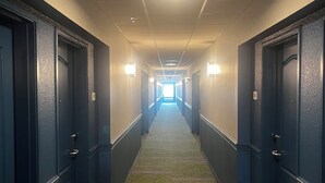 A hotel hallway with carpeted floors, blue doors, and wall-mounted lights. - Spark by Hilton Brandon (Brandon)