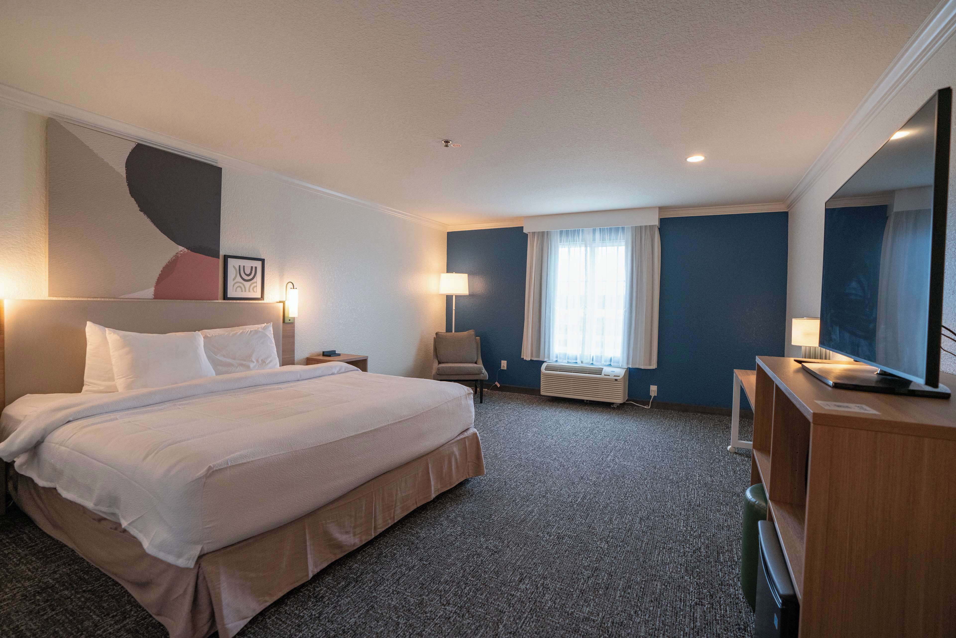 A hotel room with a large bed, a desk with a computer, a chair, and a TV.