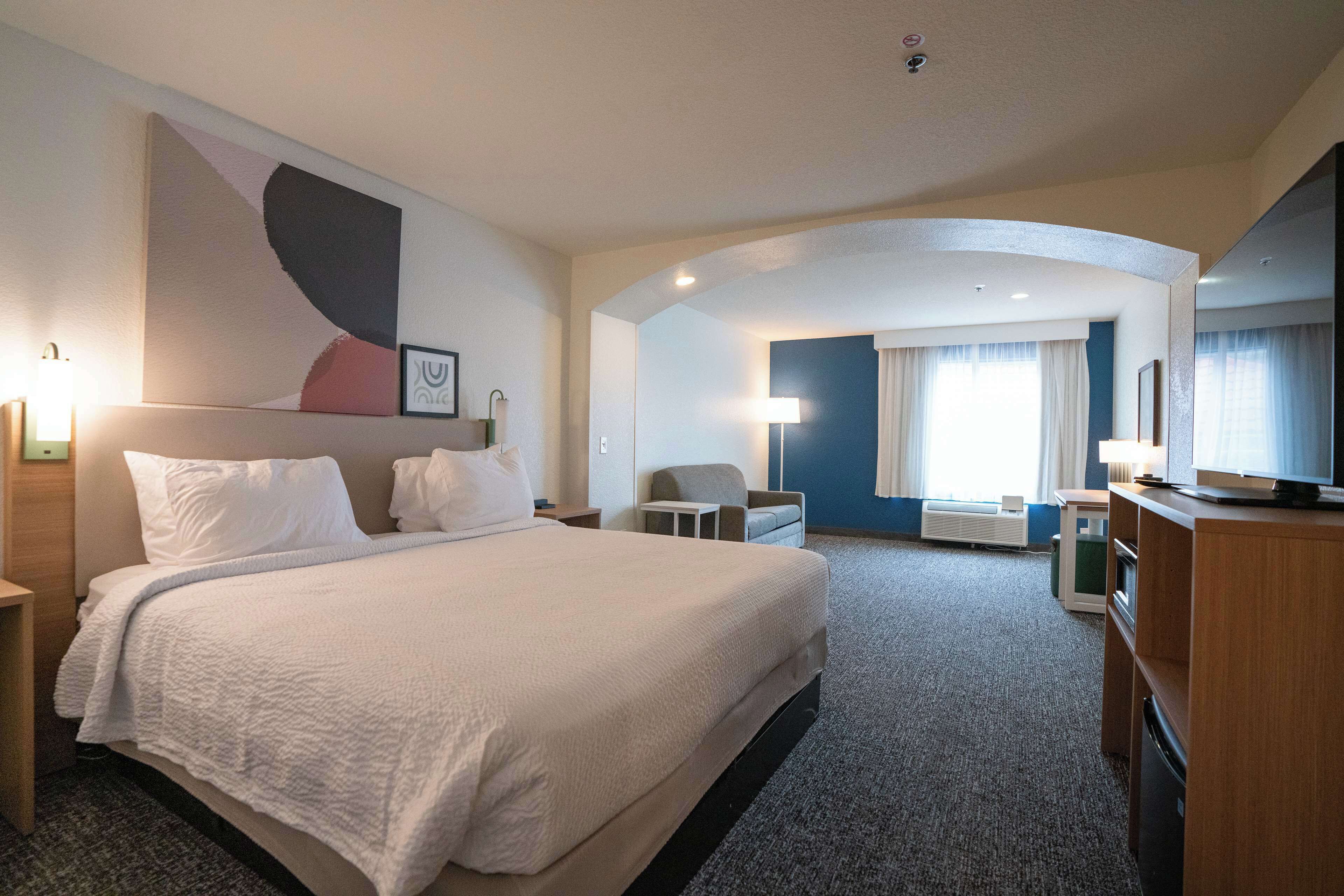 A hotel room with a large bed, a desk, a chair, a TV, and a window with curtains.