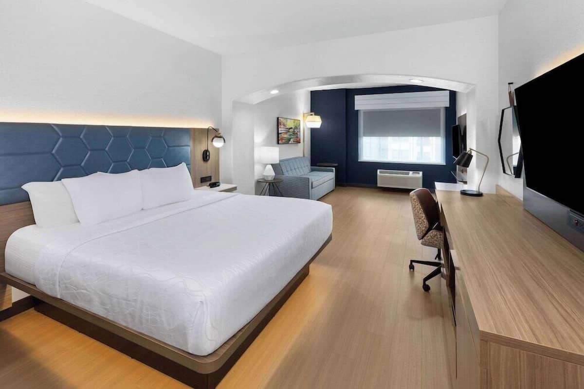 Ein modernes Hotelzimmer mit einem großen Bett, einem Schreibtisch, einem Sessel, einem Fernseher und einem Fenster.