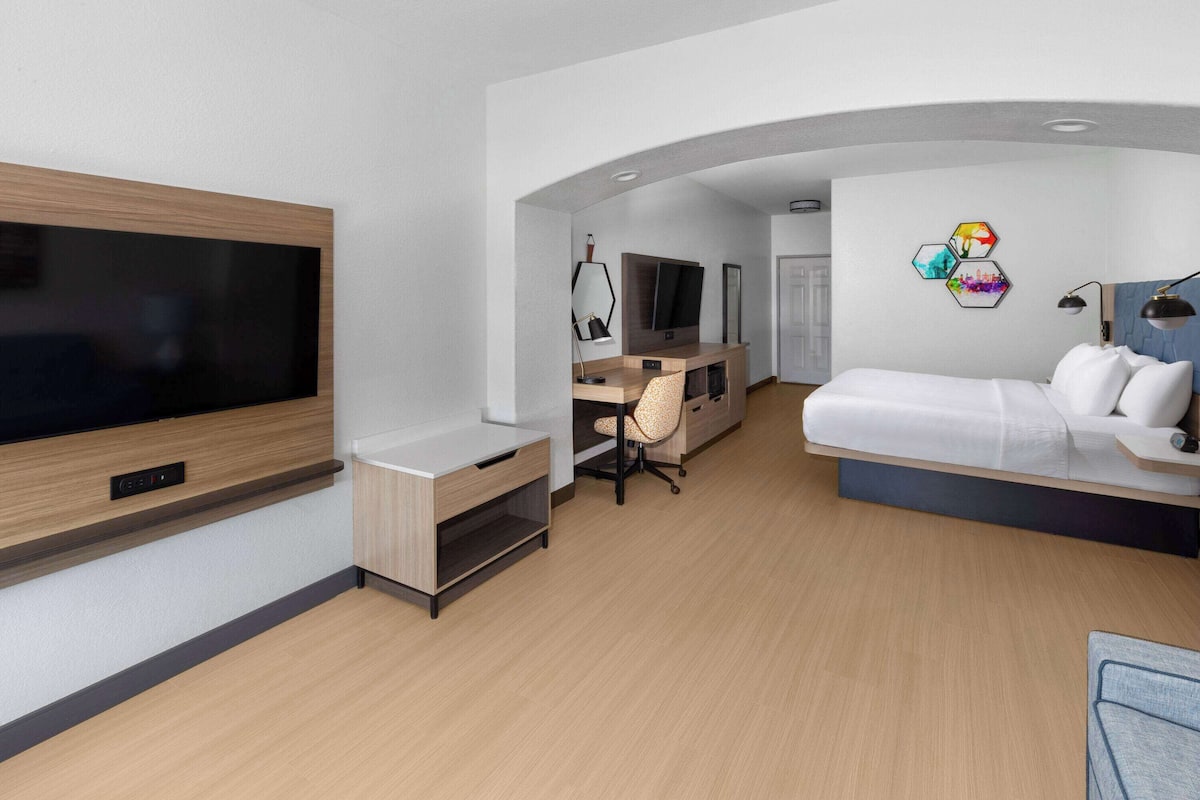 Une chambre d’hôtel moderne équipée d’une télévision à écran plat, d’un bureau avec une chaise, d’un canapé et d’un petit tapis.
