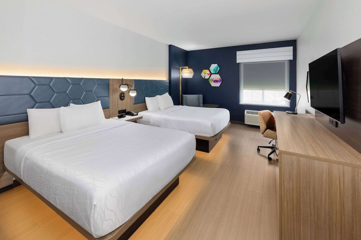 Une chambre d’hôtel avec deux lits, un bureau, une télévision et une fenêtre avec des stores.