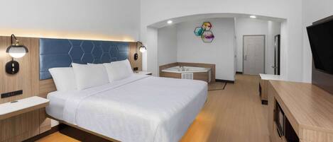 A modern hotel room with a large bed, a desk, a vanity, and a TV.