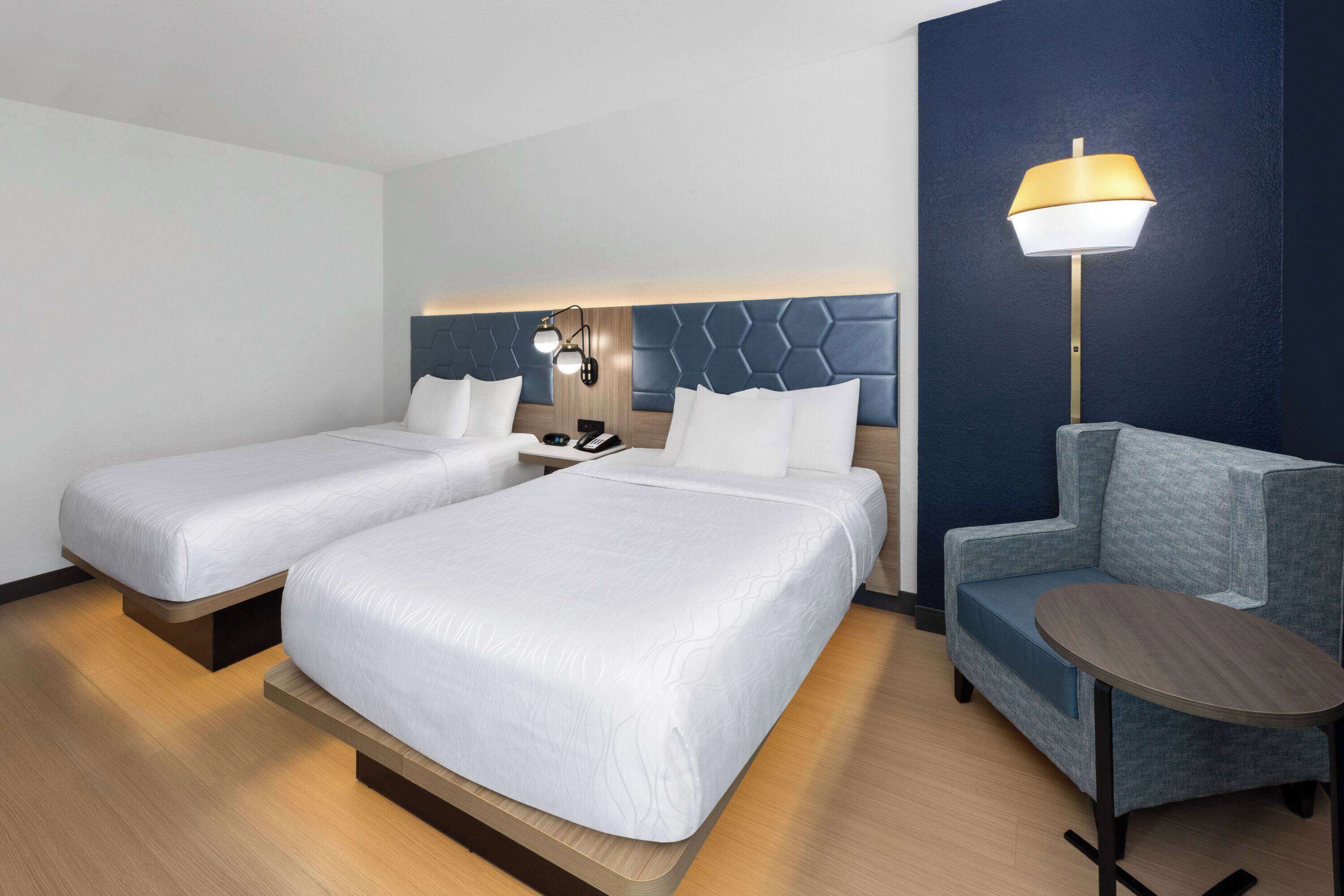 Habitación de hotel con dos camas, un escritorio, una silla y una lámpara.
